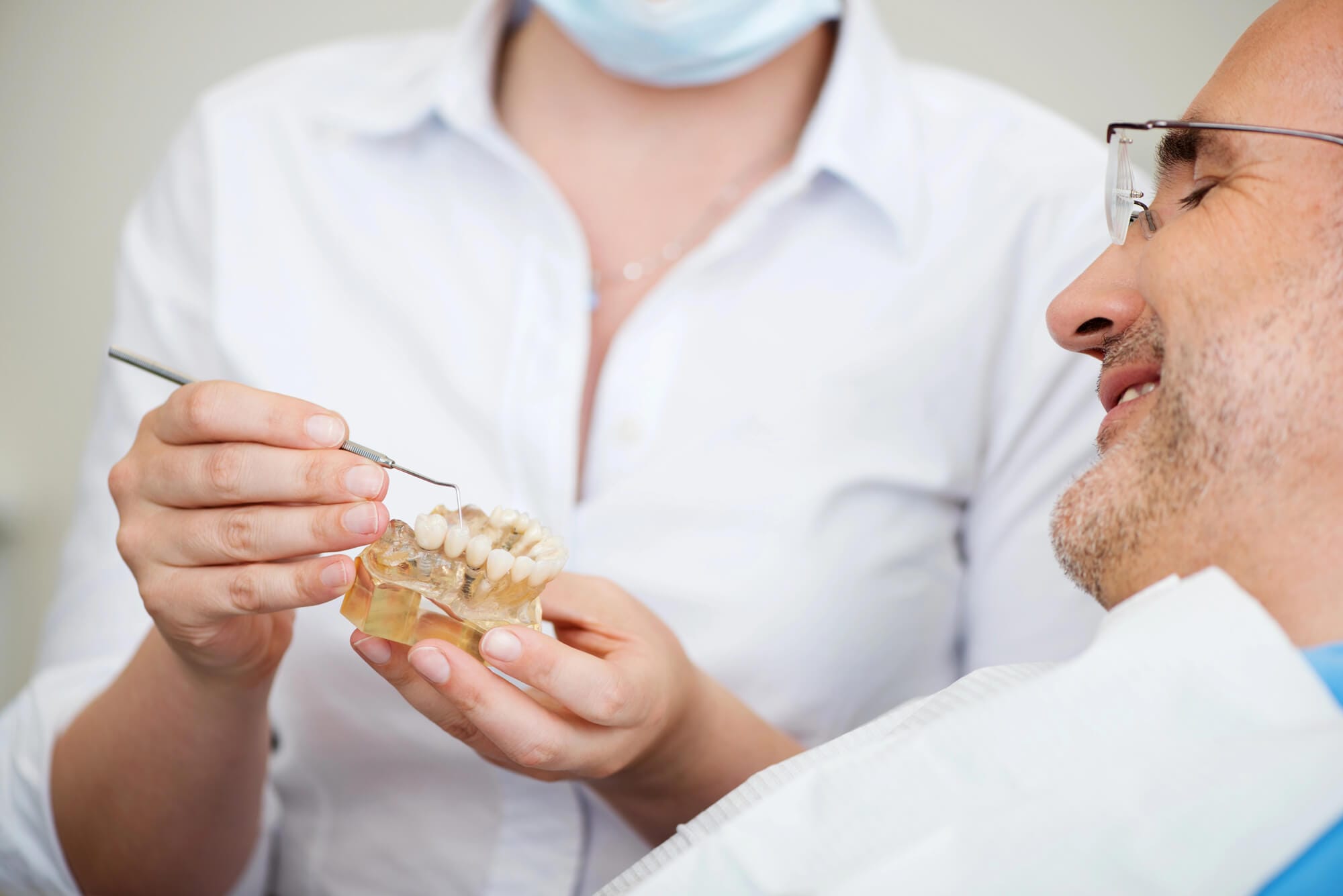 implantologia dentista a explicar a pacience como funciona um implante dentário mostrando um modelo.